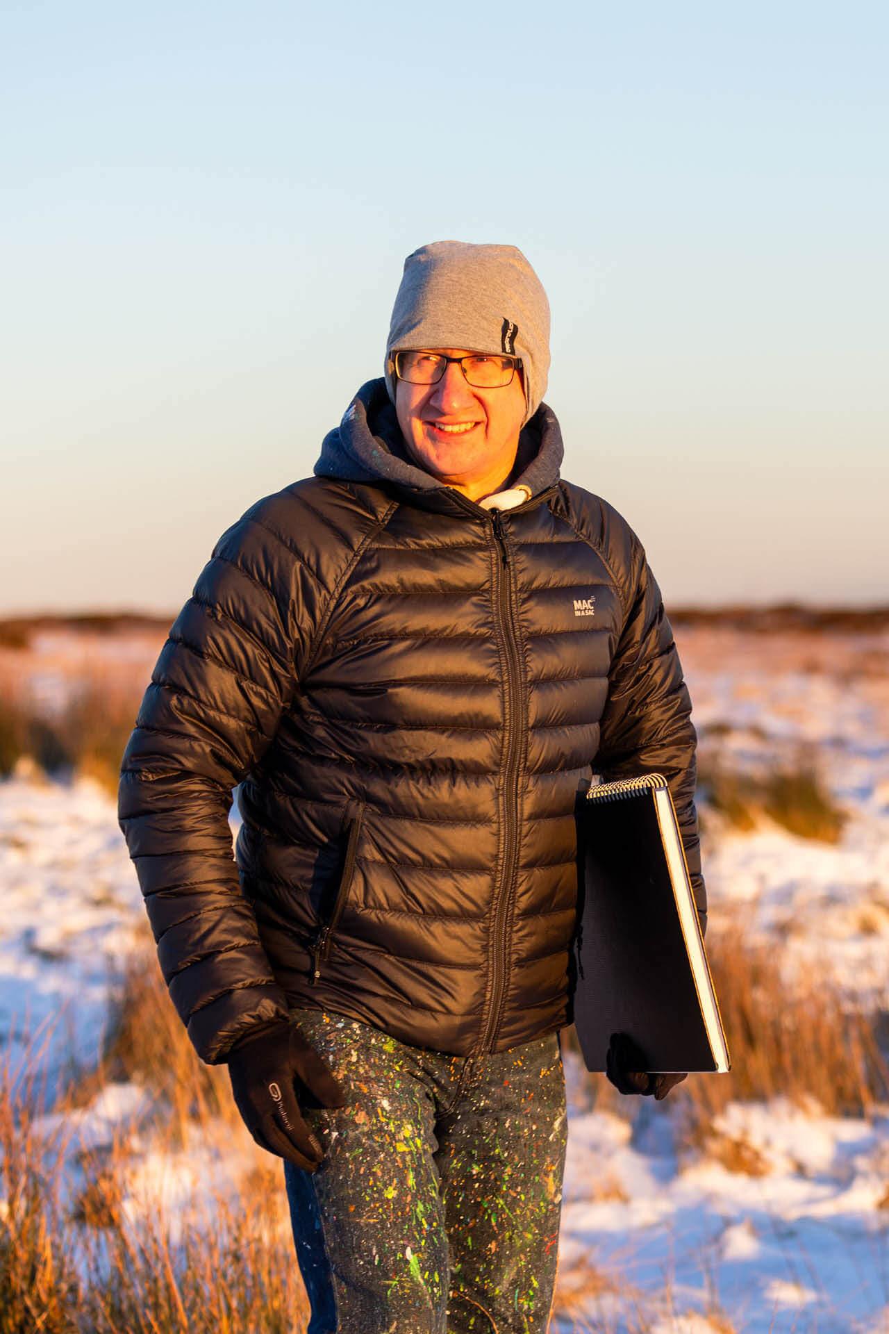 A picture of Mike Hall from MJH ArtStudio on a wintry hillside, carrying a sketch book