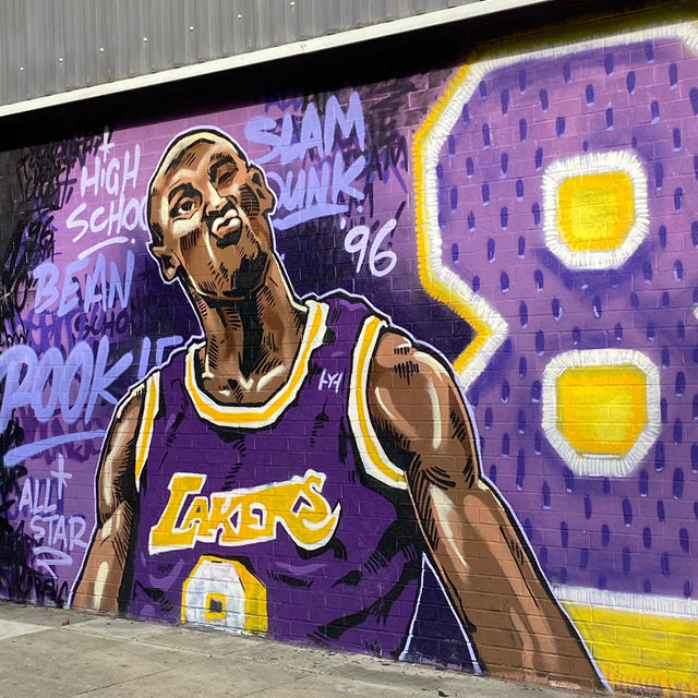 Outside wall grafitti mural artwork of basketball player using purple, lilac and yellow hues.